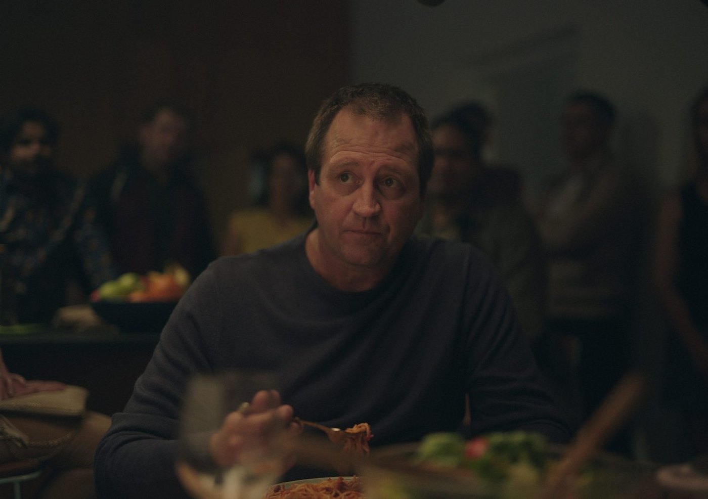 Finished frame: a man at a dinner table, listening, in warm low light