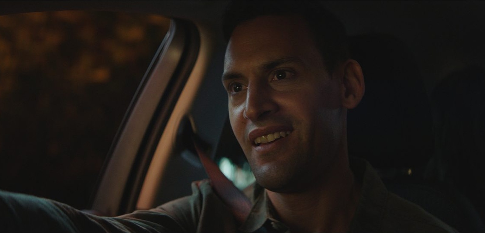 Finished frame: a driver at night, smiling, lit warm against a dark street through the side window